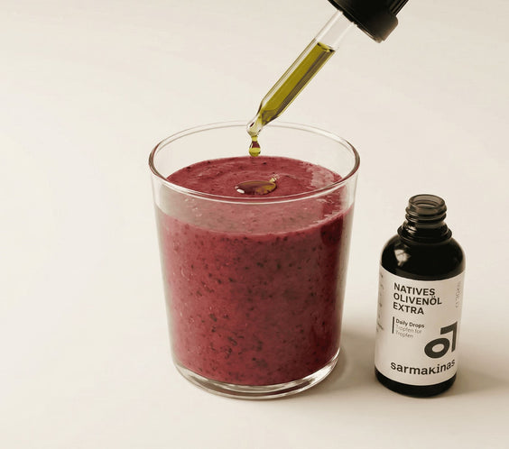 Olivenöl-Tropfen auf einem Beeren-Smoothie neben Daily-Drops-Fläschchen.