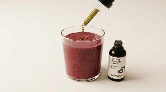 Olivenöl-Tropfen auf einem Beeren-Smoothie neben Daily-Drops-Fläschchen.