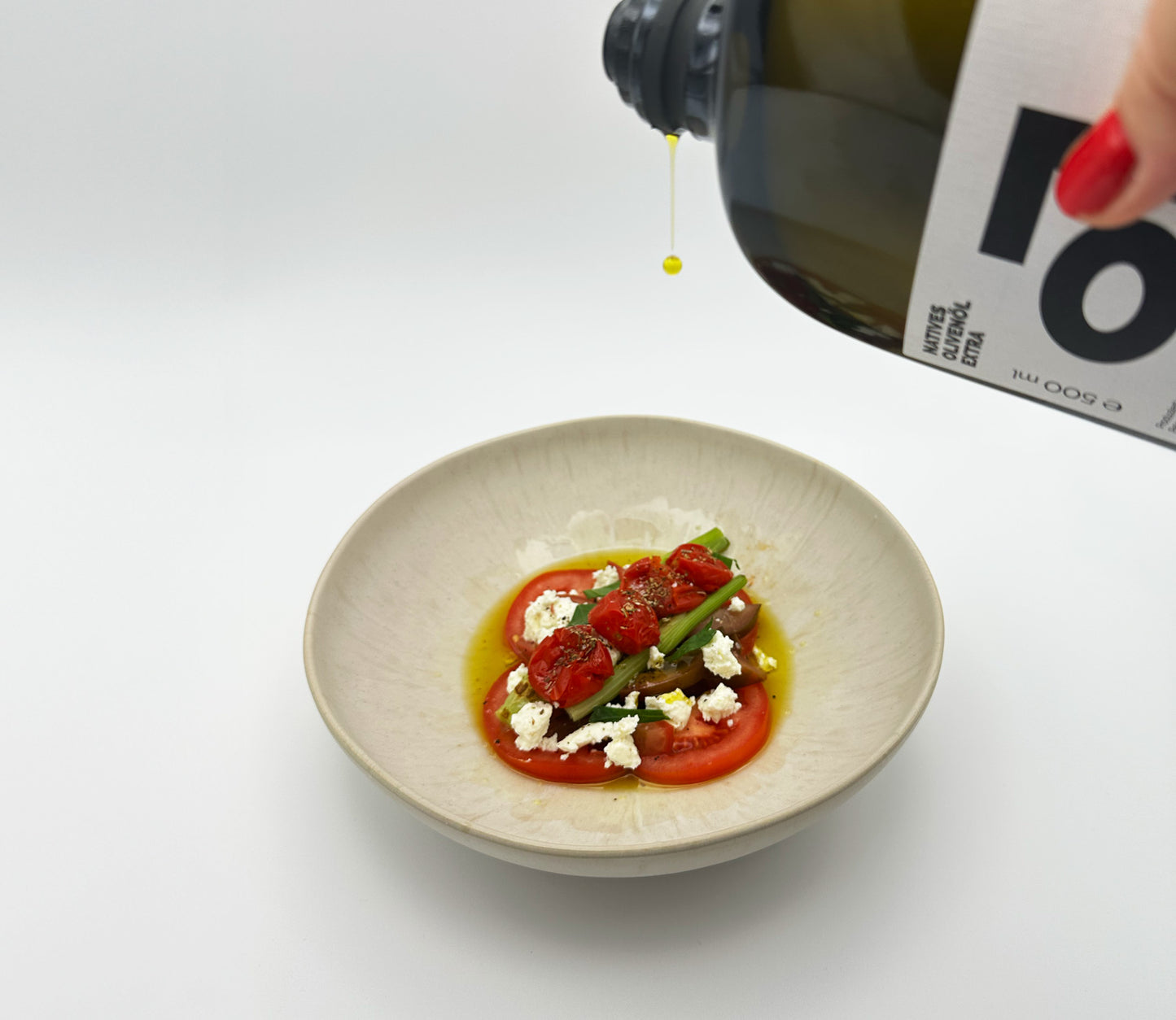 Sarmakinas Olivenöl wird langsam über einen Tomaten-Feta-Salat getropft