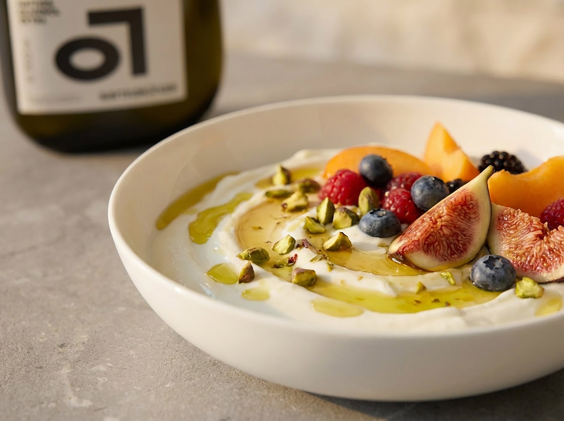 Eine weiße Schale mit Joghurt und verschiedenen Früchten und Beeren garniert und mit Sarmakinas Premium Olivenöl verfeinert.